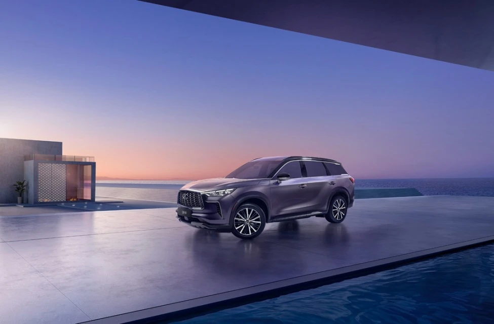 Luxury dark grey SUV car parked on a modern concrete patio near a building and overlooking the ocean at sunset with a clear sky.