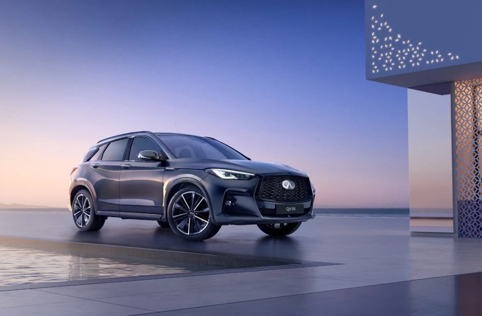 Sleek grey Infinity QX50 parked on concrete by reflective pool with modern architecture against clear blue and purple sky at dusk.