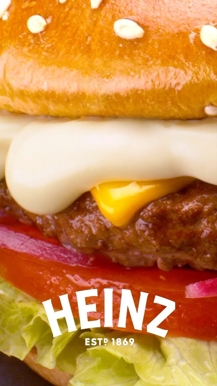 Close-up of a hamburger featuring a beef patty, cheese, lettuce, tomato, and the Heinz logo, showcasing a food and beverage image.