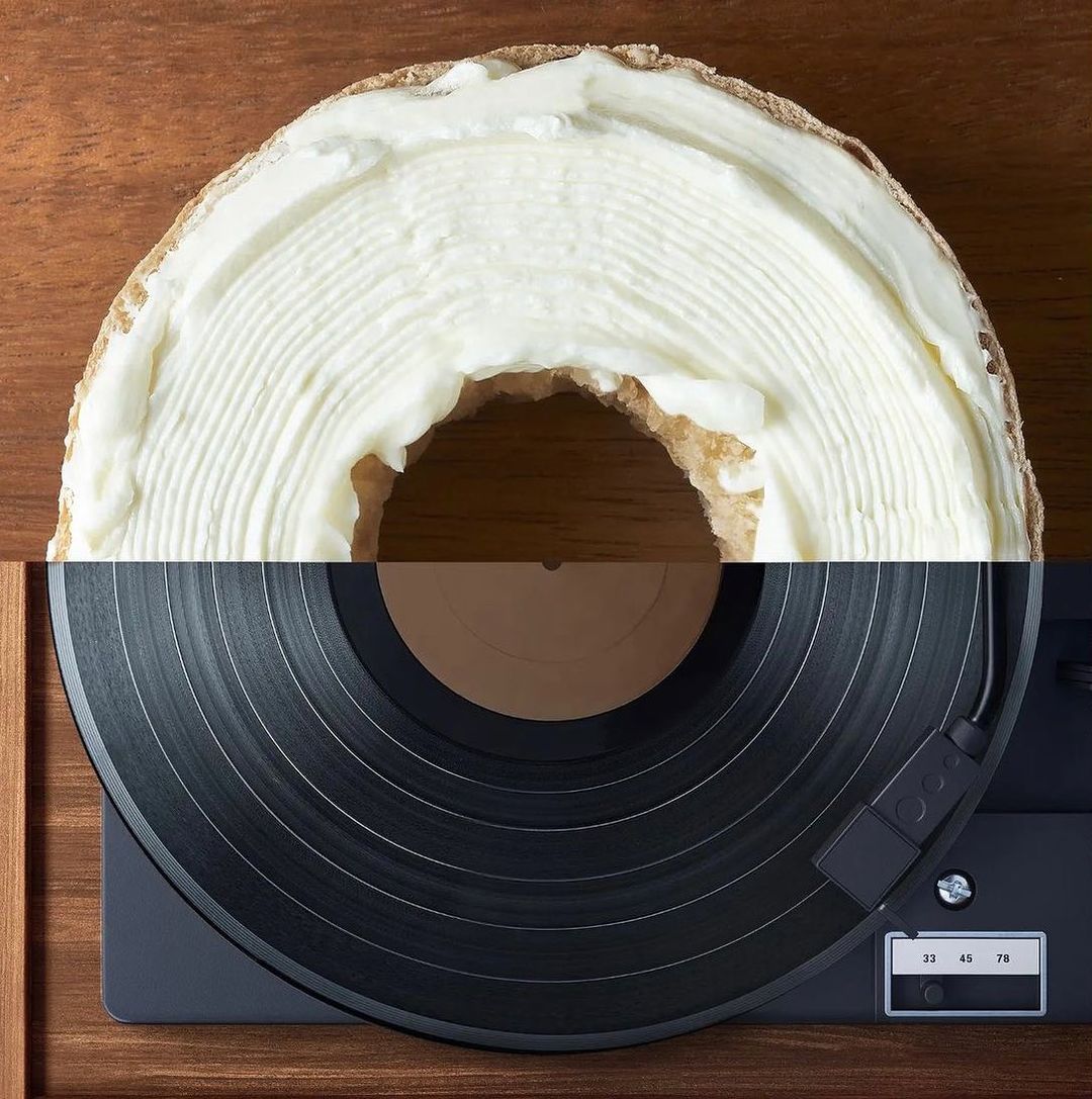 Overhead shot of a bagel with cream cheese adjacent to a vintage record player on a wood surface, creating a unique juxtaposition.