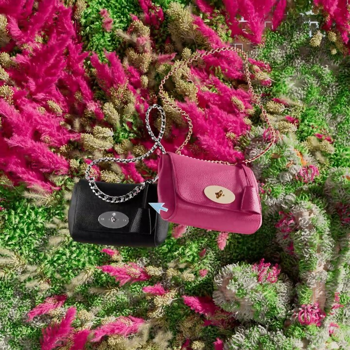 Eye-level, medium shot of two Mulberry handbags, one pink and one black, hanging against a backdrop of pink and green foliage.