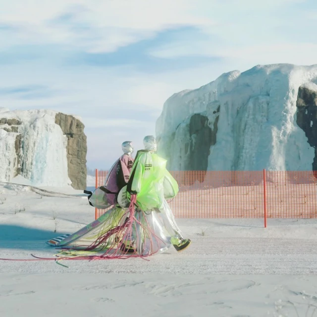 Two mannequins wear futuristic neon and iridescent outfits in a snowy arctic landscape, set against a backdrop of ice formations.