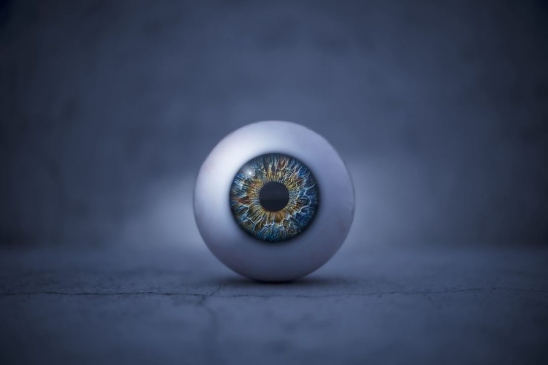 Close-up studio shot of a realistic prosthetic eye with a multicolored iris against a dark background, creating a visually striking image.
