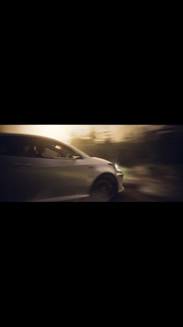 Silver car races down a dirt road with trees lining the path, captured with a motion blur effect and warm lighting.