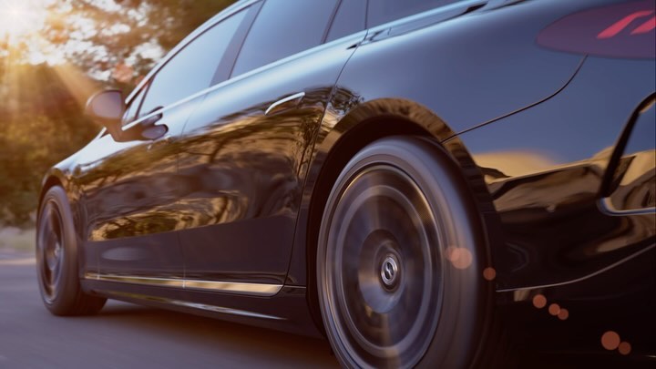 Close-up of a sleek, black, modern car moving on a road with blurred background vegetation and golden light flares.