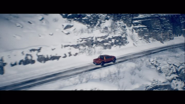 Aerial view of an orange pickup truck driving on a road through snowy mountains on a winter day. Automotive shot. 