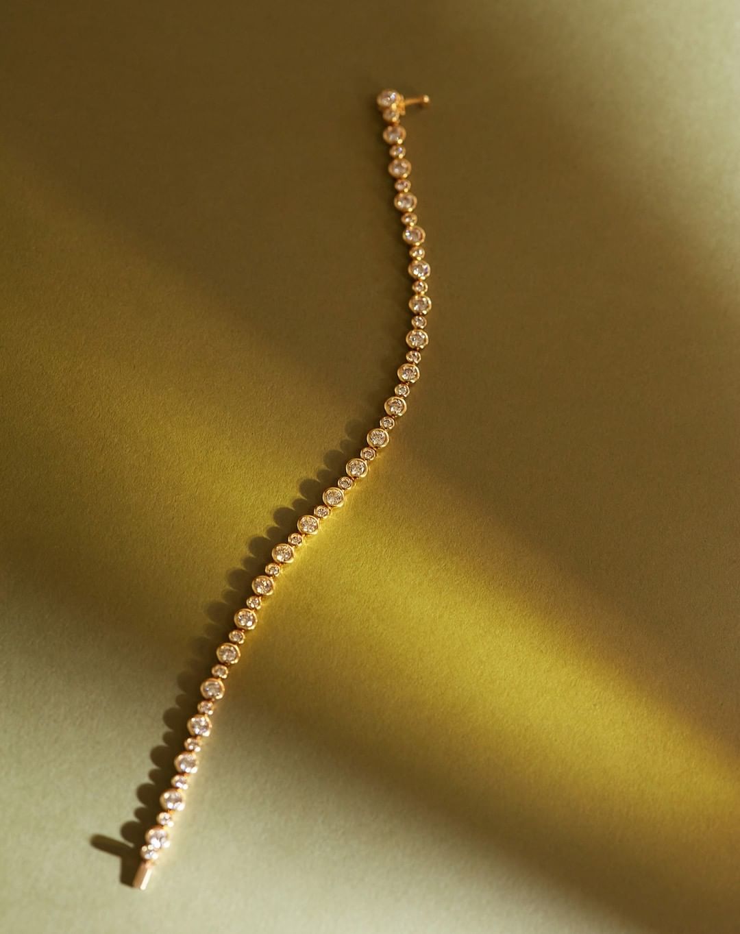 Elegant gold bracelet with sparkling diamonds on a soft, warm-toned background with cast shadows, emphasizing luxury and craftsmanship.