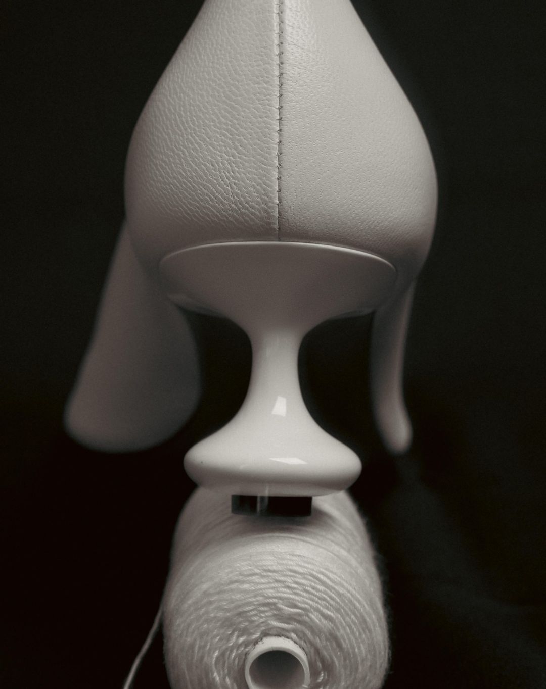 Elevated view of a white pump shoe on a black reflective surface, with a white spool of thread underneath the shoe.