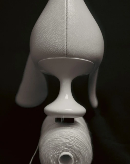 Elevated view of a white pump shoe on a black reflective surface, with a white spool of thread underneath the shoe.