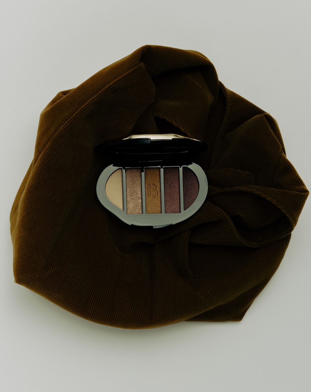 Makeup palette on a brown wrinkled cloth. Earth tones, close-up studio shot for beauty or cosmetic brand marketing.