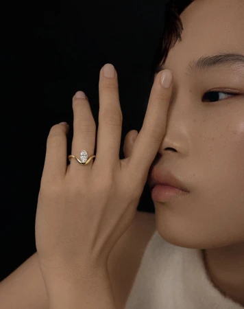 Close-up portrait of a woman holding her hand with a gold diamond ring up to her face against a black background