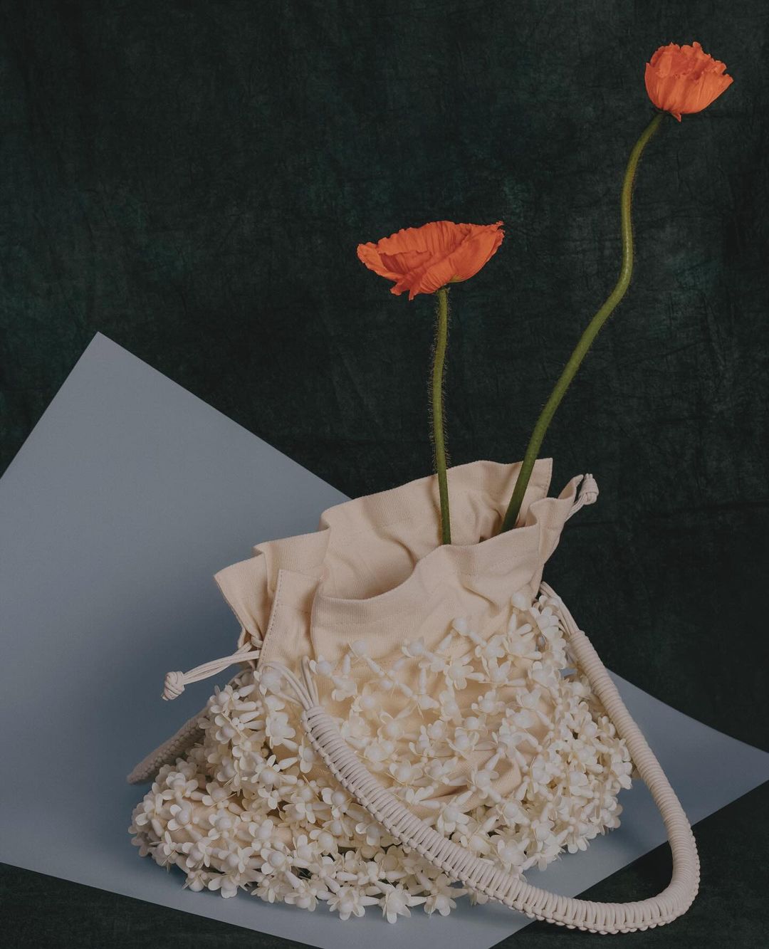 Floral handbag with orange flowers in a still life on a green and blue background. Fashion accessory with botanical elements.