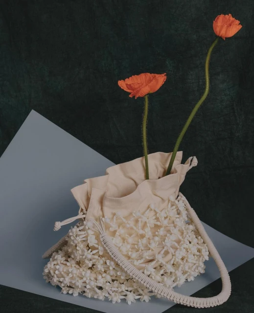 Floral handbag with orange flowers in a still life on a green and blue background. Fashion accessory with botanical elements.