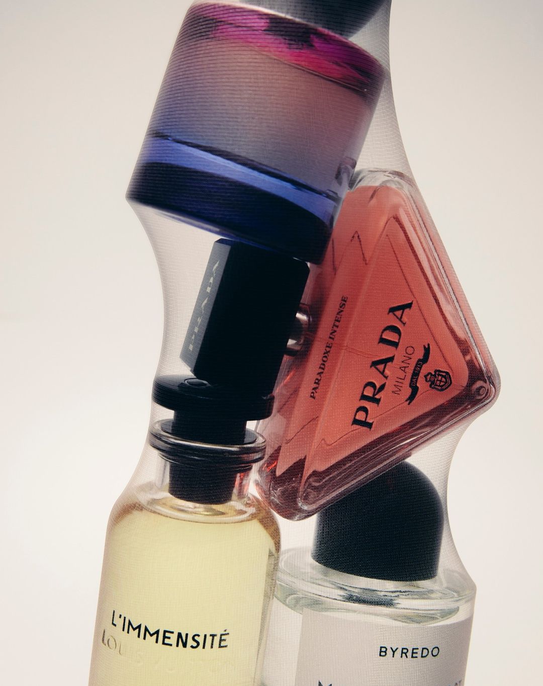Several designer fragrance bottles, including brands Prada, Byredo, and Louis Vuitton, are grouped together in a still life composition.