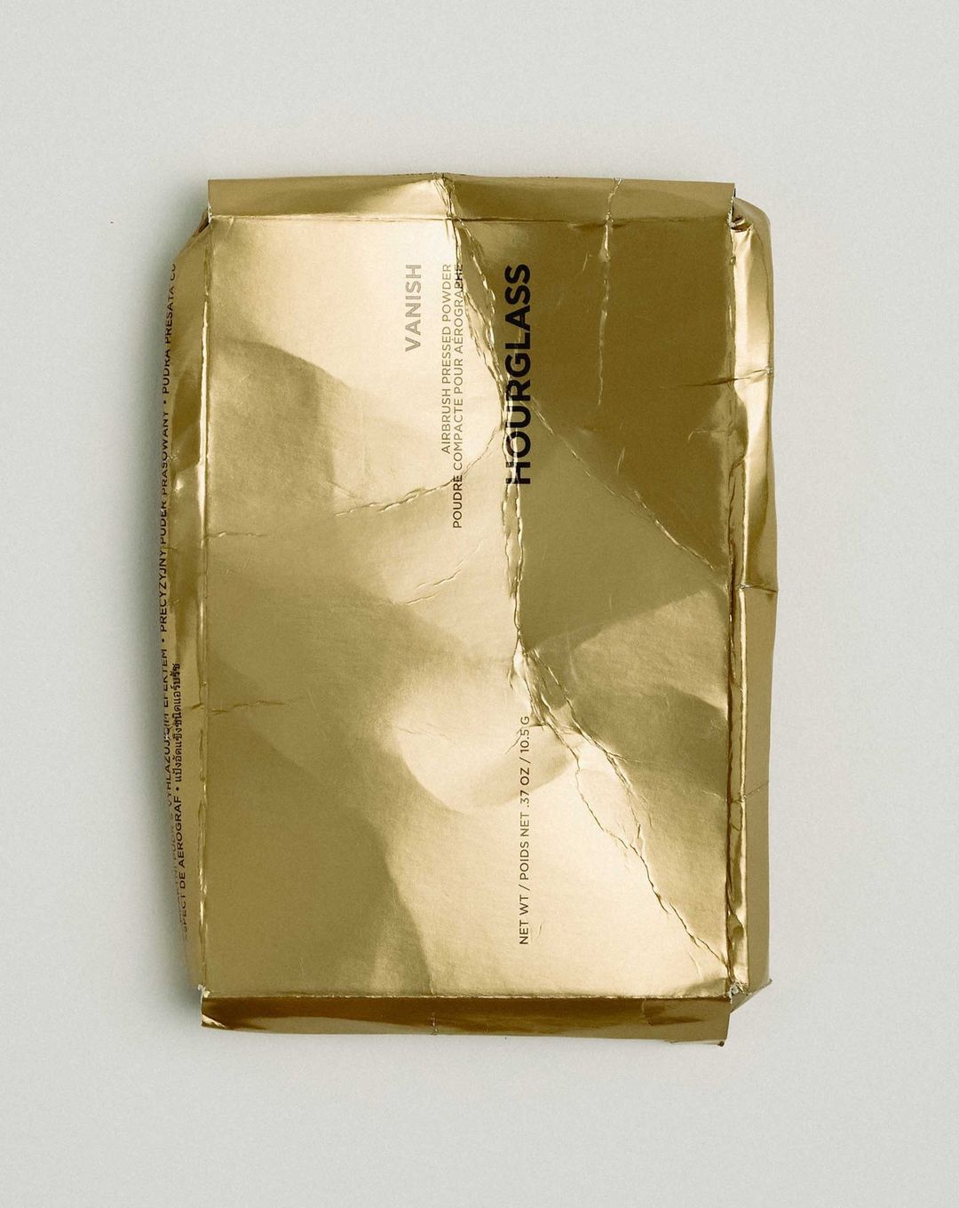 Hourglass Vanish Airbrush Pressed Powder compact packaging. Gold foil wrapper. Beauty product still life on a white surface.