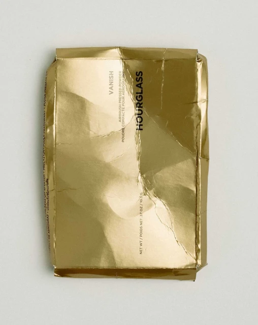Hourglass Vanish Airbrush Pressed Powder compact packaging. Gold foil wrapper. Beauty product still life on a white surface.