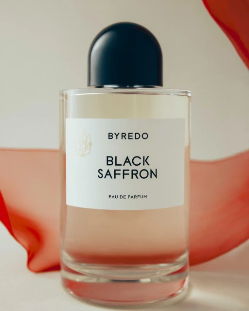 Close-up of a glass Byredo perfume bottle with a black cap and white label that reads 'Black Saffron Eau de Parfum' against a soft background.
