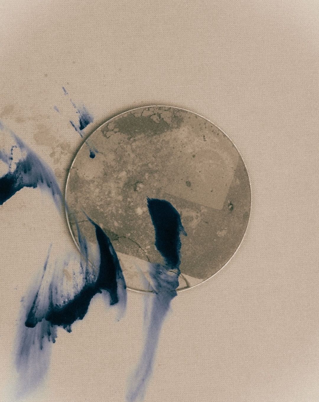 Abstract art featuring a textured circular shape with indigo-colored ink washes against a neutral background, in a conceptual style.