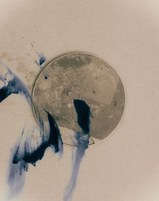 Abstract art featuring a textured circular shape with indigo-colored ink washes against a neutral background, in a conceptual style.
