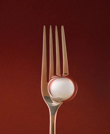 A close-up of a fork holding a white spherical object against a red background, creating a minimalist food or kitchenware image.