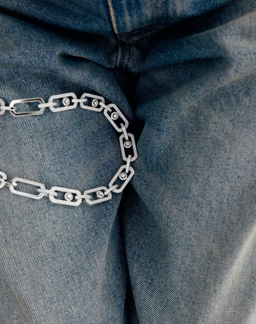 A close-up of a silver chain necklace with circular accents, draped over a pair of light blue denim jeans.