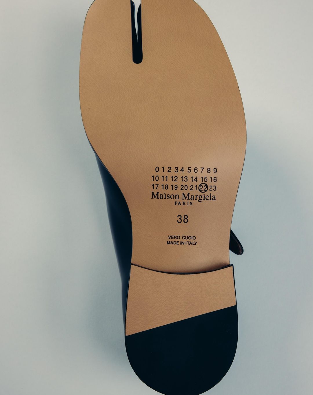 Black Maison Margiela Tabi shoe with split toe detail and stamped logo on the sole, studio shot for fashion product photography.