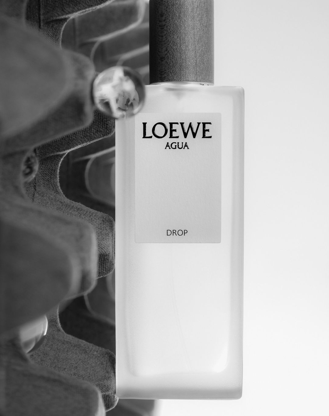 Monochromatic shot of Loewe Agua Drop perfume bottle against an egg carton, featuring a clean design and minimalist aesthetic.