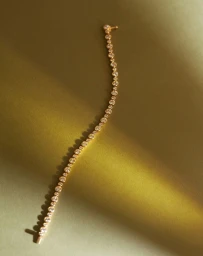 Delicate gold diamond tennis bracelet curving vertically across a textured olive green surface with soft lighting.
