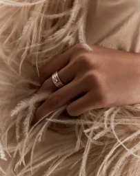 Close-up of a gold ring with a central diamond worn on a hand resting against soft cream feathers.