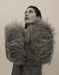 Portrait of a woman wearing a feathered top looking upward against a plain background in Paris