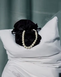 Pearl necklace draped over a black silk pouch resting on white pillows