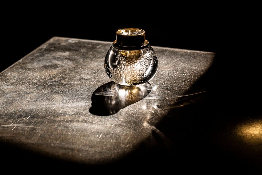 Artistic still life shot of a decorative glass bottle with golden accents, set against a dark background on a textured surface.