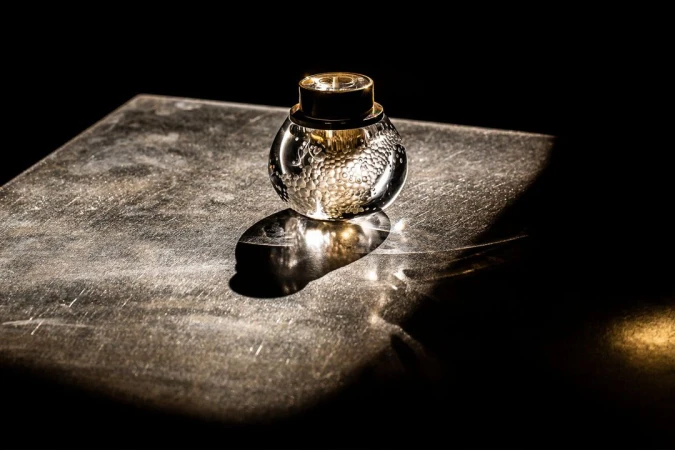 Artistic still life shot of a decorative glass bottle with golden accents, set against a dark background on a textured surface.