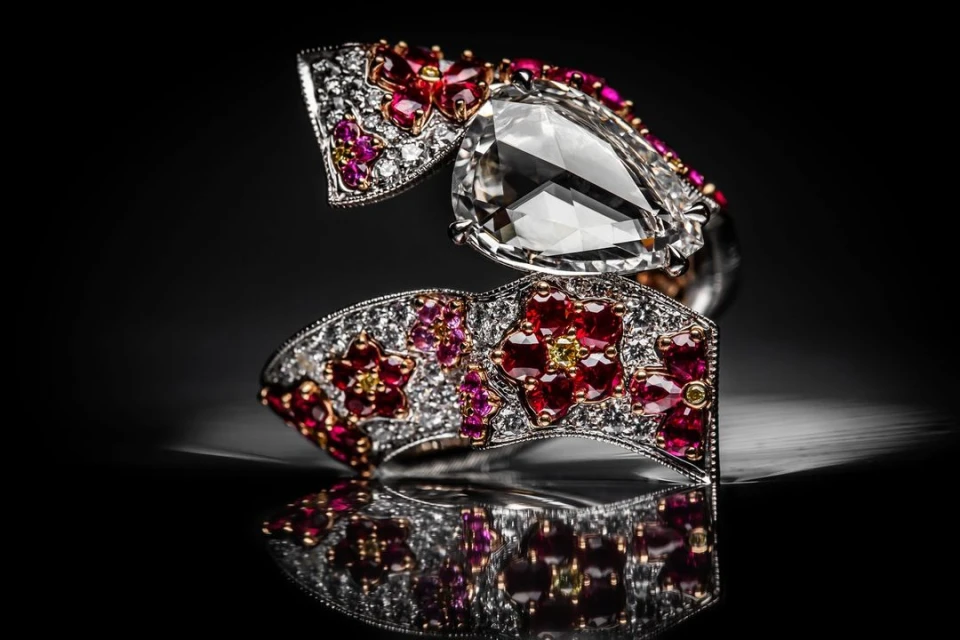 Elegant coil ring with a large pear-shaped diamond and floral gemstone embellishments, showcased against a glossy black backdrop.