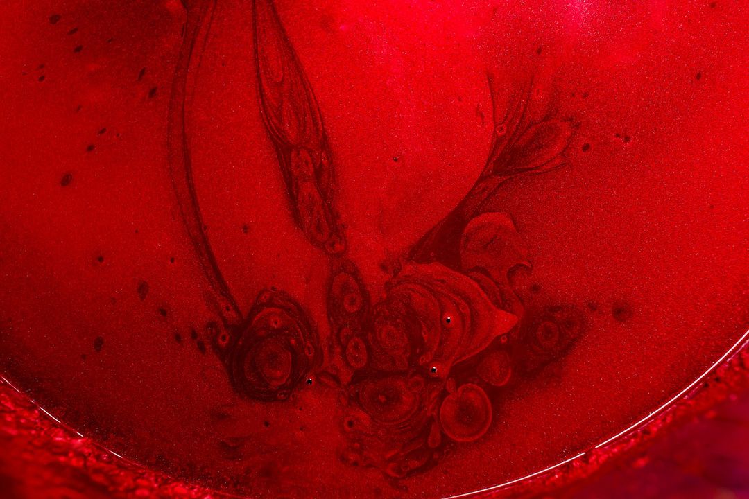 Abstract close-up of dark red liquid with swirling patterns, highlighting textures and color variations in an artistic display.