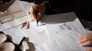 Close-up shot of a person drawing on white paper with a black pen, surrounded by sketches and design tools, showcasing artistic creation.