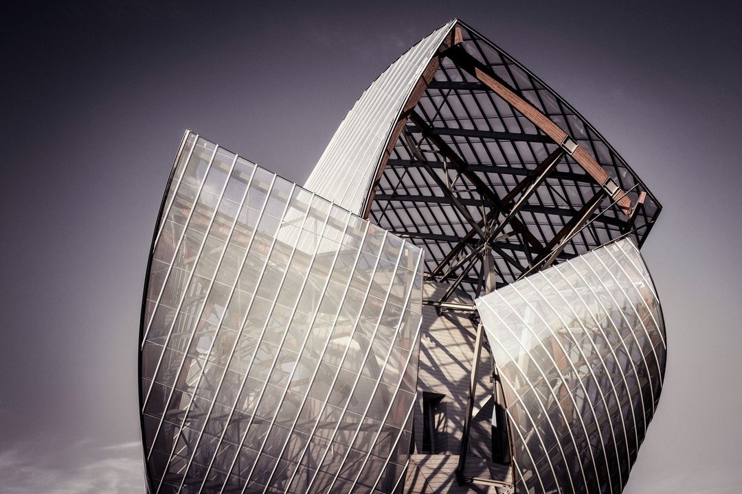 Modern glass and steel architecture with geometric design against a dramatic sky, showcasing innovative building structure.