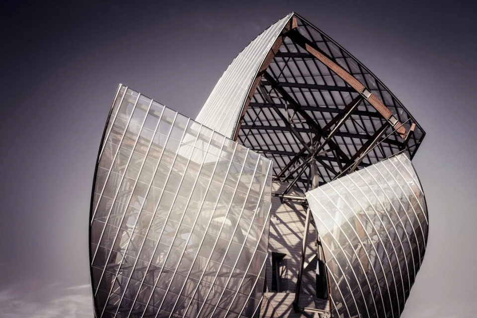 Modern glass and steel architecture with geometric design against a dramatic sky, showcasing innovative building structure.