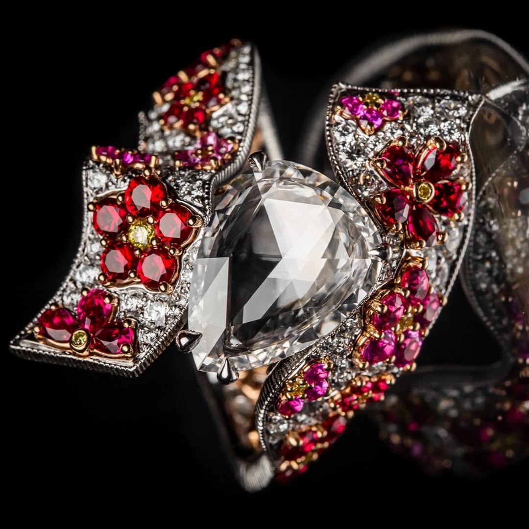 Close-up of an ornate gemstone ring featuring a large, clear pear-shaped stone surrounded by smaller red, pink, yellow, and white gems.