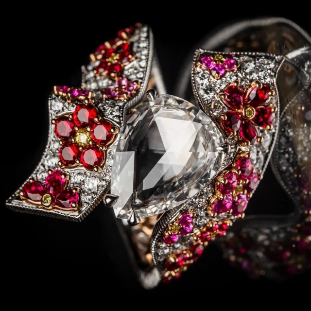 Close-up of an ornate gemstone ring featuring a large, clear pear-shaped stone surrounded by smaller red, pink, yellow, and white gems.