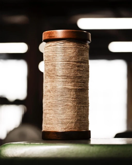 Close-up of a spool of jute twine with wooden ends placed on a green surface, set against a blurred background with soft lighting.