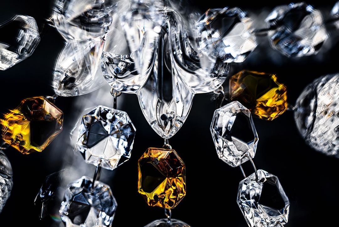 Close-up of crystal chandelier with clear and gold-tinted faceted prisms against a dark background, showcasing its intricate design.