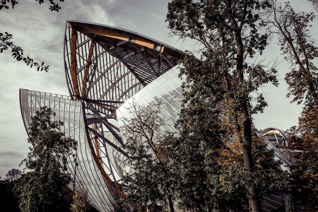 Exterior view of the Fondation Louis Vuitton in Paris, a modern architectural building surrounded by trees and foliage, captured in overcast lighting.