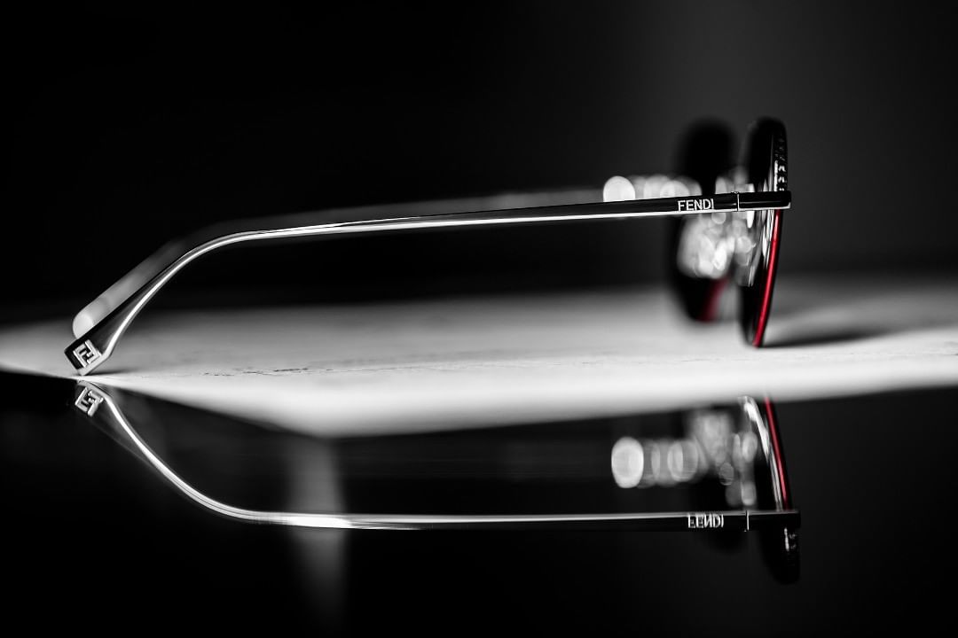 Fendi eyeglasses are displayed with a shiny surface, reflecting in a studio setting with a dark background, highlighting their design and brand.