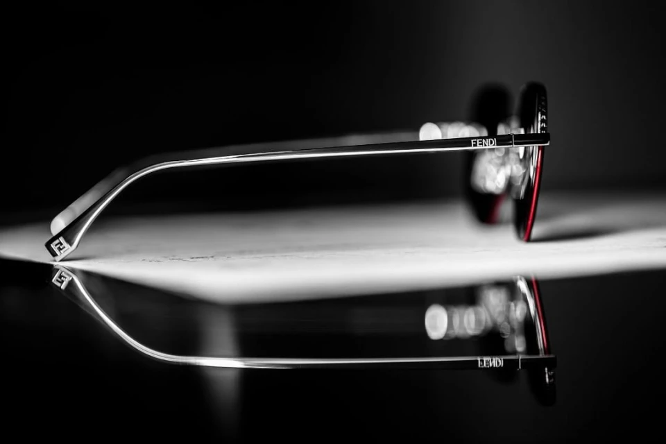 Fendi eyeglasses are displayed with a shiny surface, reflecting in a studio setting with a dark background, highlighting their design and brand.