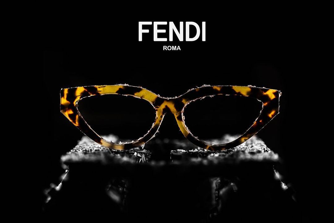 Elegant Fendi eyeglasses with a tortoiseshell pattern sit on a reflective surface against a solid black background in a studio shot.