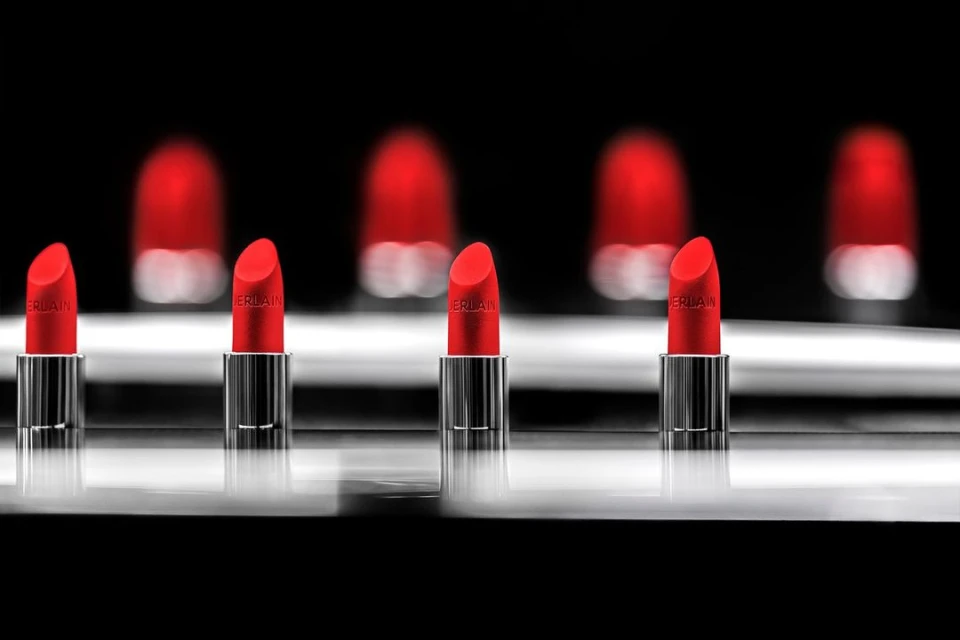 Close-up product shot of a row of red lipsticks on a reflective surface with the Guerlain logo visible against a black background.