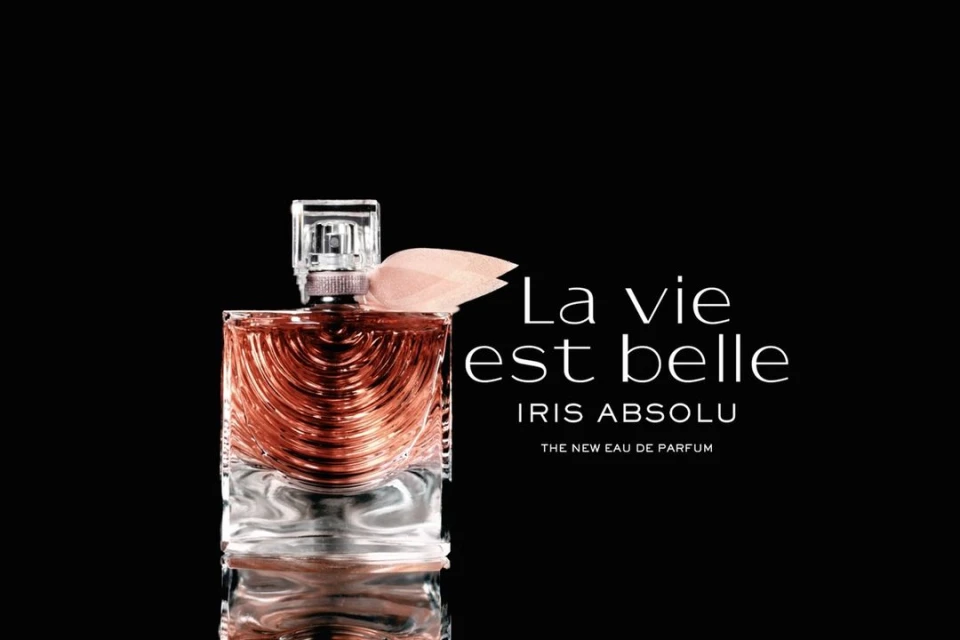 Elegant studio shot of La Vie Est Belle Iris Absolu perfume bottle against a stark black background, highlighted by soft, diffused lighting.