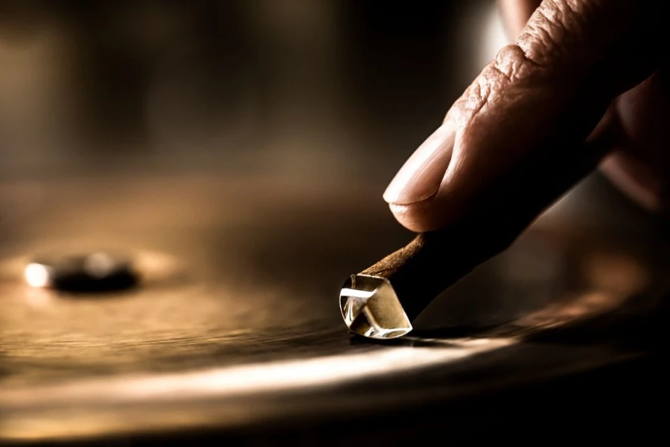 Close-up of an adult hand holding a tool with a transparent cube head resting on a golden, slightly reflective surface indoors.