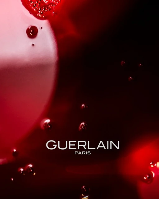 Guerlain Paris advertisement featuring a close-up of skincare product with bubbles and liquid droplets on a deep red and black background.